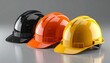 © Qaisar  - Three glossy construction safety helmets in black, orange, and yellow side by side on neutral background.