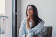 © Daniel - Pensive young woman smiling gently and looking away at copy space, happy female lost in thought daydreaming at home, planning or thinking about something, standing in living room interior