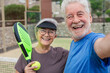 © Daniel - Old senior couple outdoors in paddle tennis court smiling and looking at the camera taking a selfie picture together playing padel. Active mature people concept