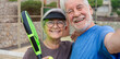 © Daniel - Old senior couple outdoors in paddle tennis court smiling and looking at the camera taking a selfie picture together playing padel. Active mature people concept