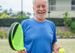 © Daniel - One old mature senior man in padel court outdoors looking at the camera having fun holding paddle tennis racquet smiling and enjoying after game