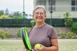 © Daniel - One old mature senior woman in padel court outdoors looking at the camera having fun holding paddle tennis racquet smiling and enjoying after game