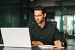 © Stock 4 You - Portrait of young adult European man wearing eyeglasses looking at laptop screen. Motivated latin student writing notes during lesson, watching webinar, learning online, sitting at work desk in office