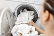 © wedmoments.stock - Woman with long hair loading a washing machine with white laundry, demonstrating the process of doing laundry in a modern home environment with clean appliances
