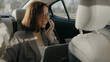 © tol_u4f - Woman talking on phone and working on laptop in back seat of car during daytime in a city environment