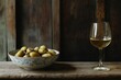 © mehaniq41 - Glass of white wine beside bowl of green olives on rustic wooden table. Soft lighting, dark blurred background, earthy ambiance captured. Neural network AI generated
