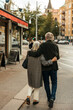 © Maskot - Rear view of senior couple walking with arm around each other while spending leisure time at city street