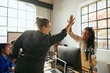 © Maskot - Cheerful female business expert giving high-five to colleague during meeting in tech office