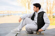 © Pixel-Shot - Young man in grey sports suit sitting on skateboard outdoors