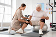 © Pixel-Shot - Senior man with therapist putting on knee pads in rehabilitation center