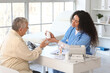 © Pixel-Shot - Young African-American doctor giving pill bottle to senior woman at table in clinic