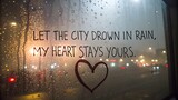 A heartfelt message of enduring love written on a rain-streaked window overlooking a blurry city night