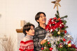 © Kawee - Asian loving father and young son decorate Christmas tree in house.