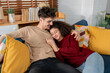 © Kawee - Latina young couple sitting together on sofa in living room at home.