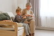 © sementsova321 - A child and an older woman sit together on a comfortable sofa, happily engaged in knitting. The warm atmosphere highlights their joyful connection
