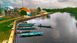 © AmazingAerialAgency - Aerial view of boats with vibrant colors resting by the waterfront near buildings with orange roofs under a cloudy sky, Abonnema, Port Harcourt, Nigeria.