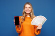 © ViDi Studio - Young woman in yellow sweater casual clothes use blank screen mobile cell phone hold in hand fan of cash money in dollar banknotes isolated on plain blue background studio portrait Lifestyle concept