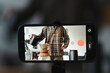 © Studio Marmellata - A person in a plaid shirt films a video of brewing pour-over coffee using a smartphone on a stand. The phone's screen shows the live footage of the coffee preparation.