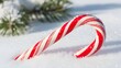 © Eka - A classic red and white striped candy cane lies in soft, fresh white snow, evoking the sweet essence of holiday celebrations and winter charm, with a hint of green pine