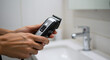 © Photyn Studio - A hand holds an electric hair clipper in a bathroom, highlighting modern grooming technology.Concept of personal grooming and modern device technology.