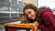 © TanTin - Gently smiling teenage girl with old cat in animal shelter on woven blanket, pet adoption center