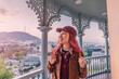 © EdNurg - Happy young woman tourist enjoying panoramic city views, standing on a traditional balcony in old Tbilisi, Georgia