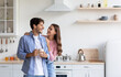 © Prostock-studio - Cheerful millennial european wife hugs husband with cup of hot drink in minimalist kitchen interior. Couple enjoy coffee together at home, breakfast in morning, copy space