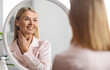 © Prostock-studio - Beautiful Middle Aged Woman Looking At Mirror And Touching Her Soft Skin On Neck, Attractive Mature Lady Smiling To Reflection, Enjoying Anti-Aging Skincare Routine At Home, Selective Focus