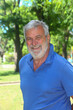 © atikinka2 - Portrait of a cheerful senior Latino man smiling outdoors with lush greenery in the background.