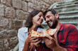 © Novak - Young couple sitting on city stairs and eating delicious pizza slices