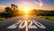 © punyapob - Road with 2026 start painted on it leading towards a bright sun on the horizon with trees and hills tree