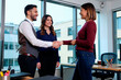 © Seventyfour - Caucasian young adult man shaking hands with young adult woman while colleague standing nearby smiling, business meeting taking place in modern office setting