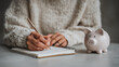 © AnastasiiaAkh - Woman planning budget and saving money with piggy bank at home