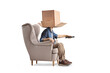 © Ljupco Smokovski - Man with cardboard box on his head sitting in armchair and using remote control