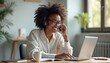 © miss irine - African woman smiles while wearing headset, typing on laptop. She is engaged in online conversation, likely remote work or customer service. Modern home office setting with plants and desk.