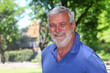 © atikinka2 - Portrait of a cheerful senior Latino man smiling outdoors with lush greenery in the background.