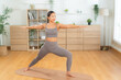 © Leny Studio - Fit Asian woman stretching in yoga pose on wooden floor, home workout and mobility training for healthy body, wellness and self-love concept in minimalism living room, authentic candid woman smiling
