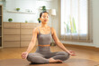 © Leny Studio - Peaceful Asian female in sportswear practicing yoga pose for harmony and balance at home, serene atmosphere with morning sun, authentic lifestyle and meditation for well-being in cozy apartment room