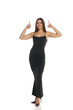 © vladimirfloyd - Studio shot of an amazed woman with dark hair wearing a long black dress and high heels, standing and pointing up with both hands, full body, on a white background