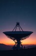 © Vadym - Large radio telescope dish silhouetted against twilight sky with stars. Mountains in distance capture dusk colors. Tech asset for space, science, or communication themes.