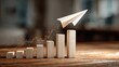 © Sawyer0 - A paper airplane rising above a wooden bar graph symbolizes rapid progress, innovation, and creative business growth.
