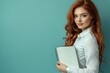 © YouraPechkin - Young woman with red hair holding notebook against blue background in a studio setting