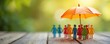 © Pete - Colorful paper people figures stand together under an open orange umbrella. Symbolizing group protection security for team members. Life and health benefit concept.