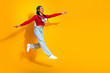 © deagreez - Young woman jumps in cap and red top against yellow background showcasing casual streetwear style and joyful energy for fashion advertising and lifestyle branding