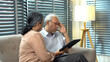 © kaew6566 - Stressed Asian senior man having headache while using digital tablet with concerned wife at home. Elderly couple facing bad news or online scam problem concept on sofa.