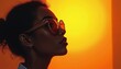 © Viktor - Dark skinned woman wears stylish sunglasses. She looks up thoughtfully against a vibrant warm orange yellow gradient background. Her profile is sharp.