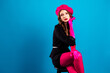 © deagreez - Chic young woman in pink beret gloves and black dress posing glamorous fashion shoot against blue backdrop