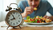 © Viktor - Man eats healthy food near alarm clock. Intermittent fasting concept meal. Time restricted eating plan for weight loss diet. Healthy lifestyle nourishment.