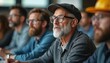 © Viktor - Mature man with beard and glasses attends technical seminar. Diverse adult males listen attentively in classroom setting, learning new skills for career.