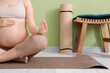 © Pixel-Shot - Sporty pregnant woman meditating on mat near green wall at home